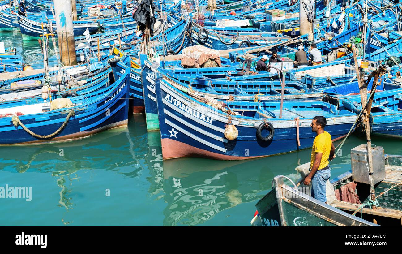Essaouira, Maroc - 17 septembre 2022 : pêcheurs à bord de bateaux de pêche bleus amarrés au port d'Essaouira. Les bateaux de pêche bordent le port, amenant dans la da Banque D'Images