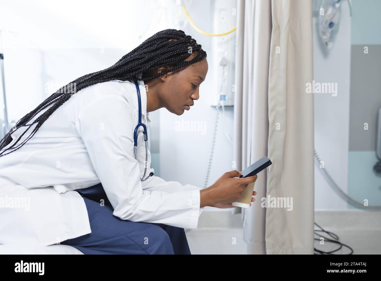 Femme médecin afro-américaine assise sur le lit à l'aide d'un smartphone à l'hôpital Banque D'Images