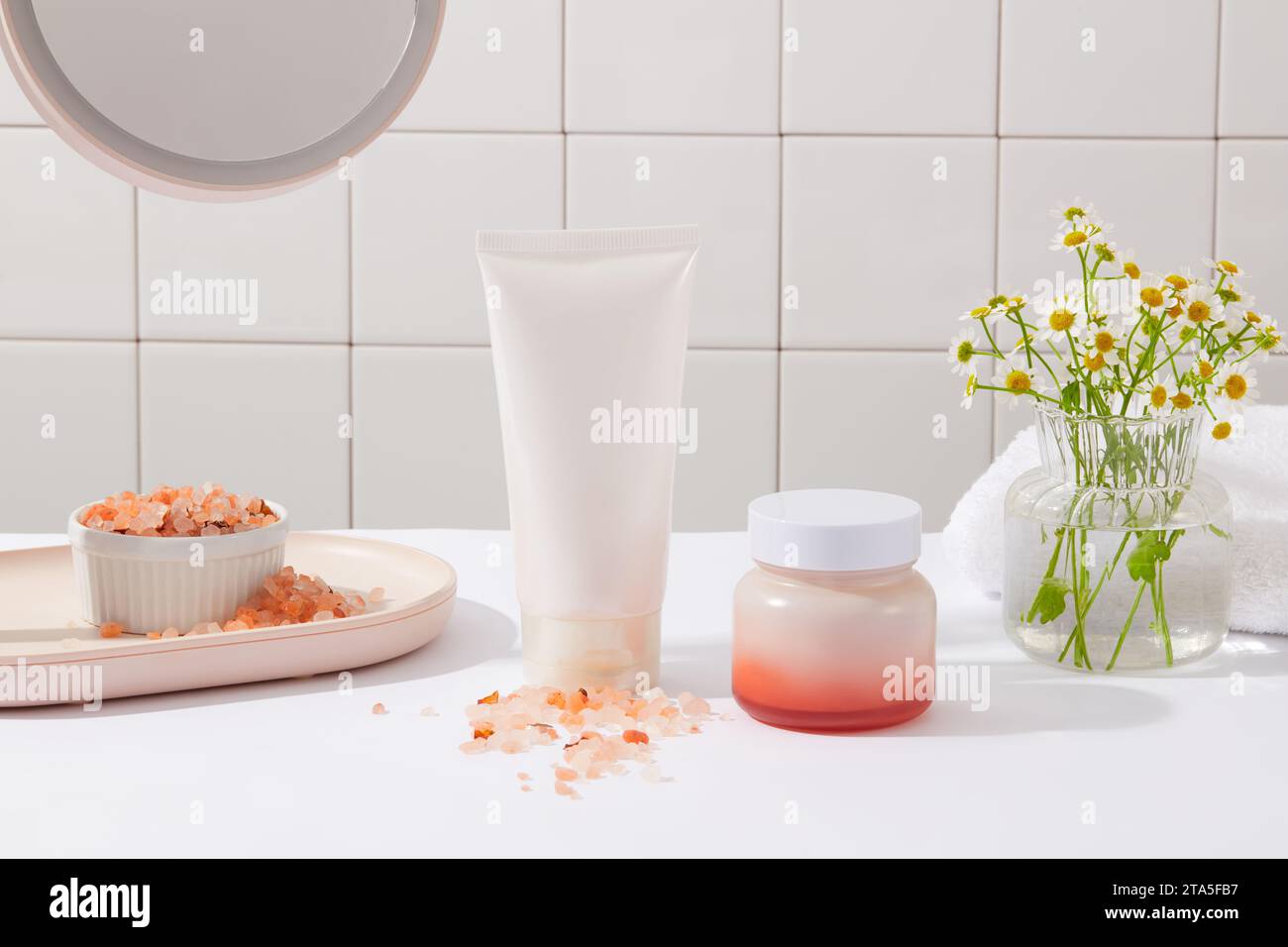Vue de face d'un tube blanc et pot sans étiquette disposés avec un bol de sel rose de l'himalaya et pot de fleurs. Le sel rose de l'Himalaya est un type de sel tha Banque D'Images