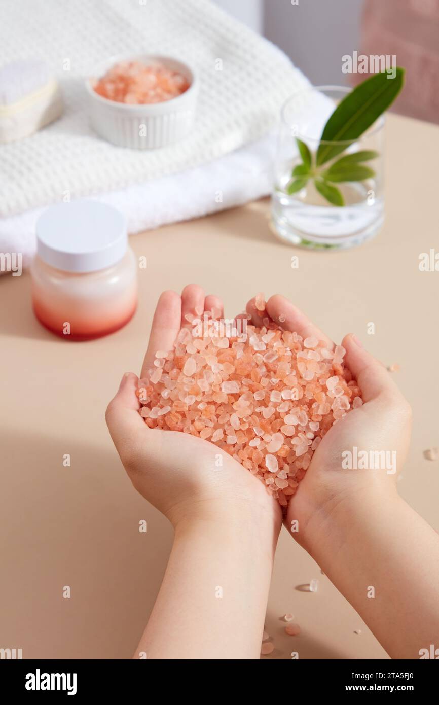 Un tas de sel rose de l'himalaya entre les mains. Pot cosmétique sans étiquette affichée. Le sel rose de l'himalaya peut améliorer les conditions de la peau et apaiser les douleurs musc Banque D'Images