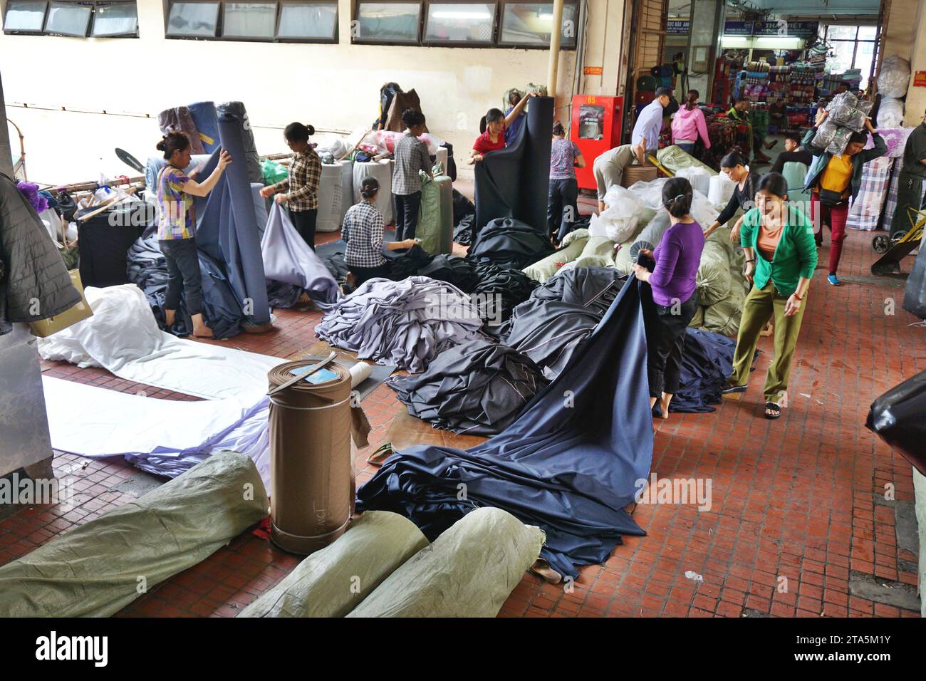 Les travailleurs mesurent d'énormes rouleaux de tissu sur un marché de gros textile à Hanoi, Vietnam. Les bobines massives de tissu sont réduites à une taille plus gérable Banque D'Images