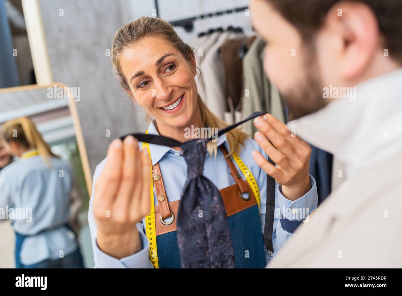 Femme sur mesure ajustant une cravate pour un client avec un sourire dans un magasin de mariage Banque D'Images