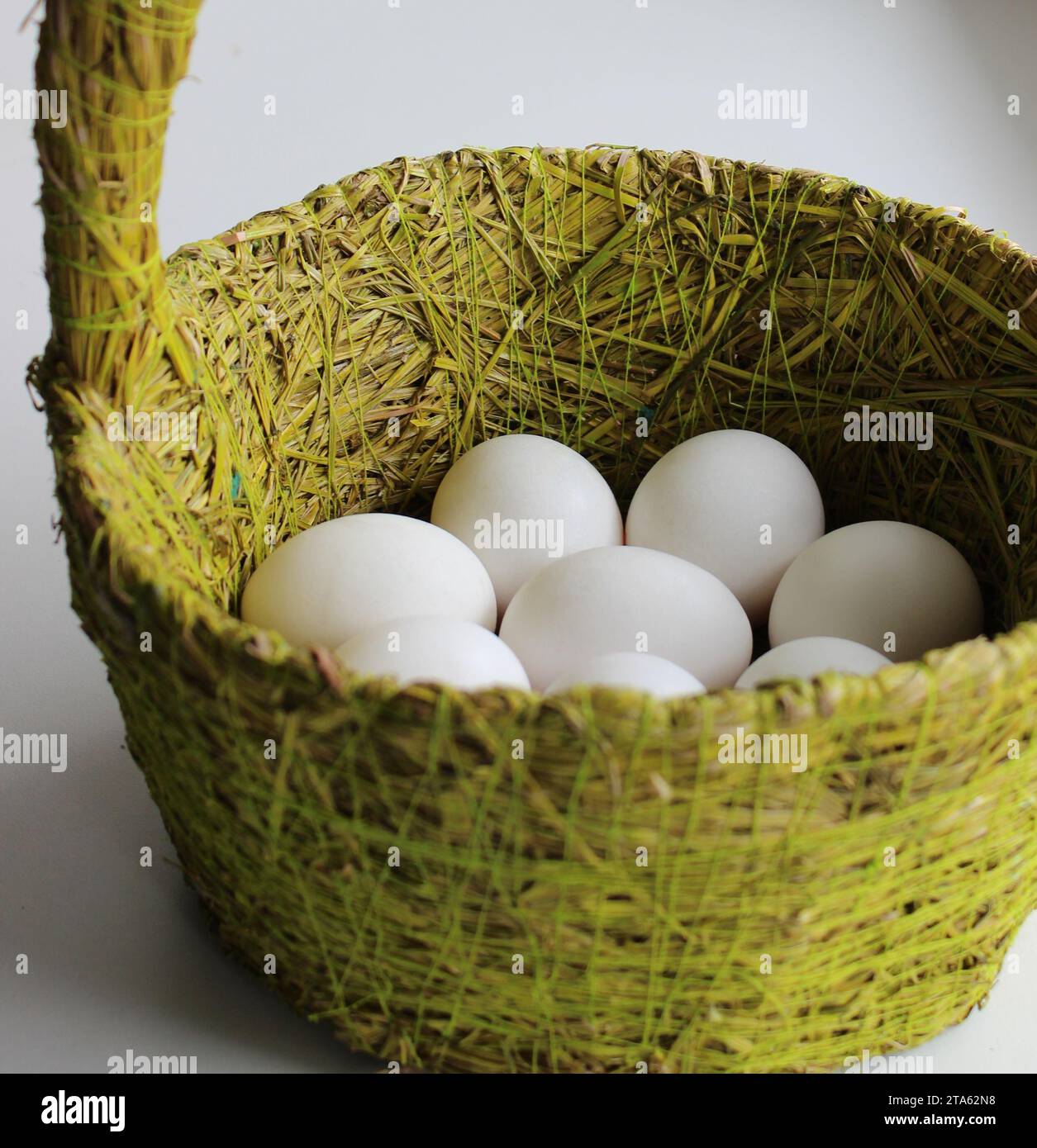 Panier tissé avec des fibres d'herbe avec des œufs de poulet entiers blancs Banque D'Images