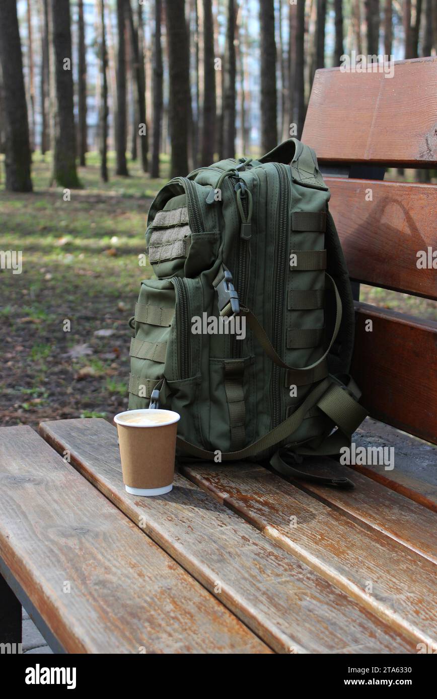 Une tasse de café à côté d'un sac à dos appuyé contre le dos d'un banc en bois Banque D'Images