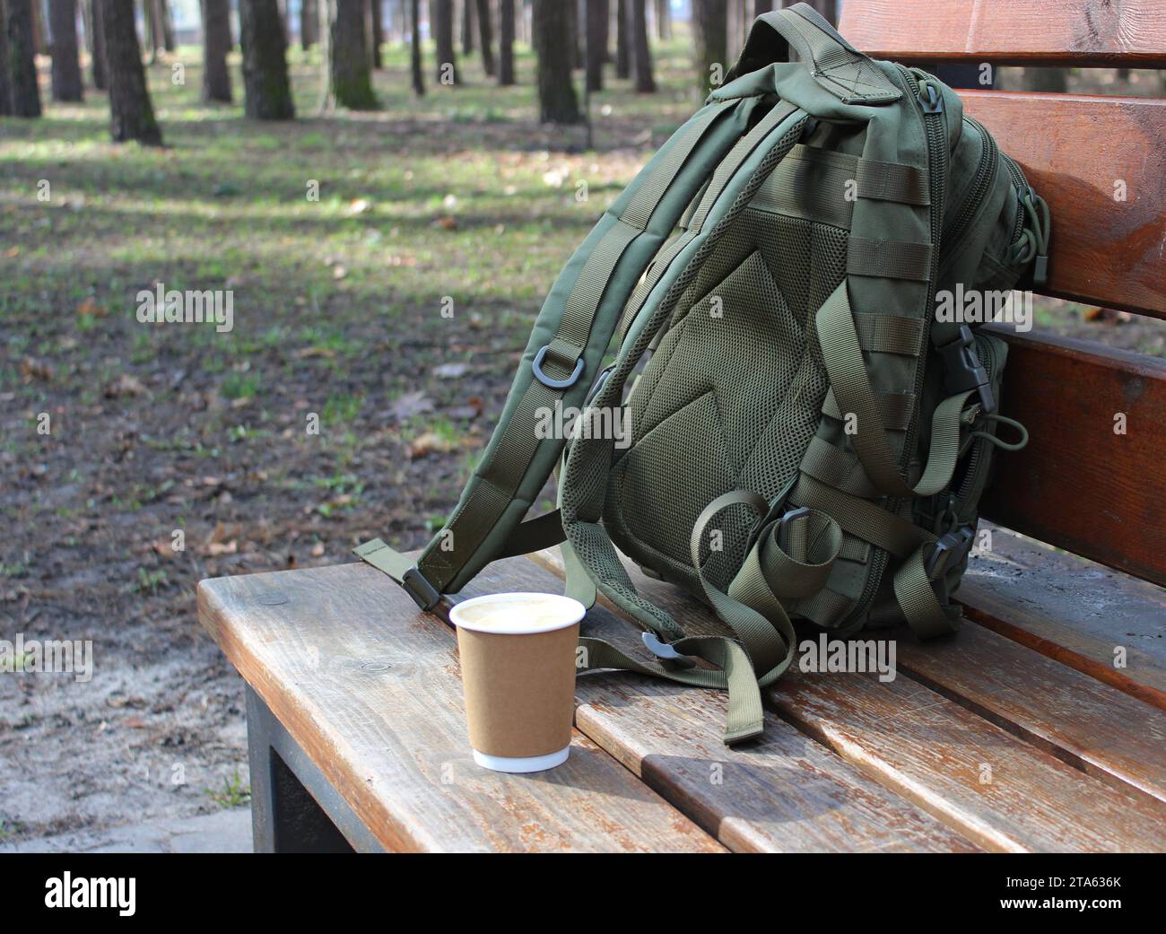 Tasse de café artisanale et un sac à dos sur un banc en bois dans un parc de la ville comme symboles du début d'un voyage Banque D'Images