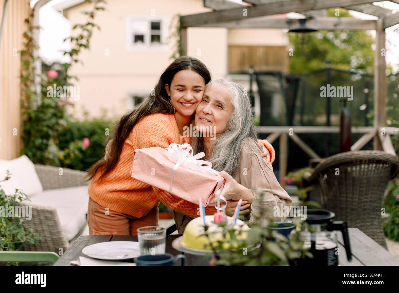 Fille heureuse embrassant et donnant cadeau d'anniversaire à grand-mère au patio Banque D'Images