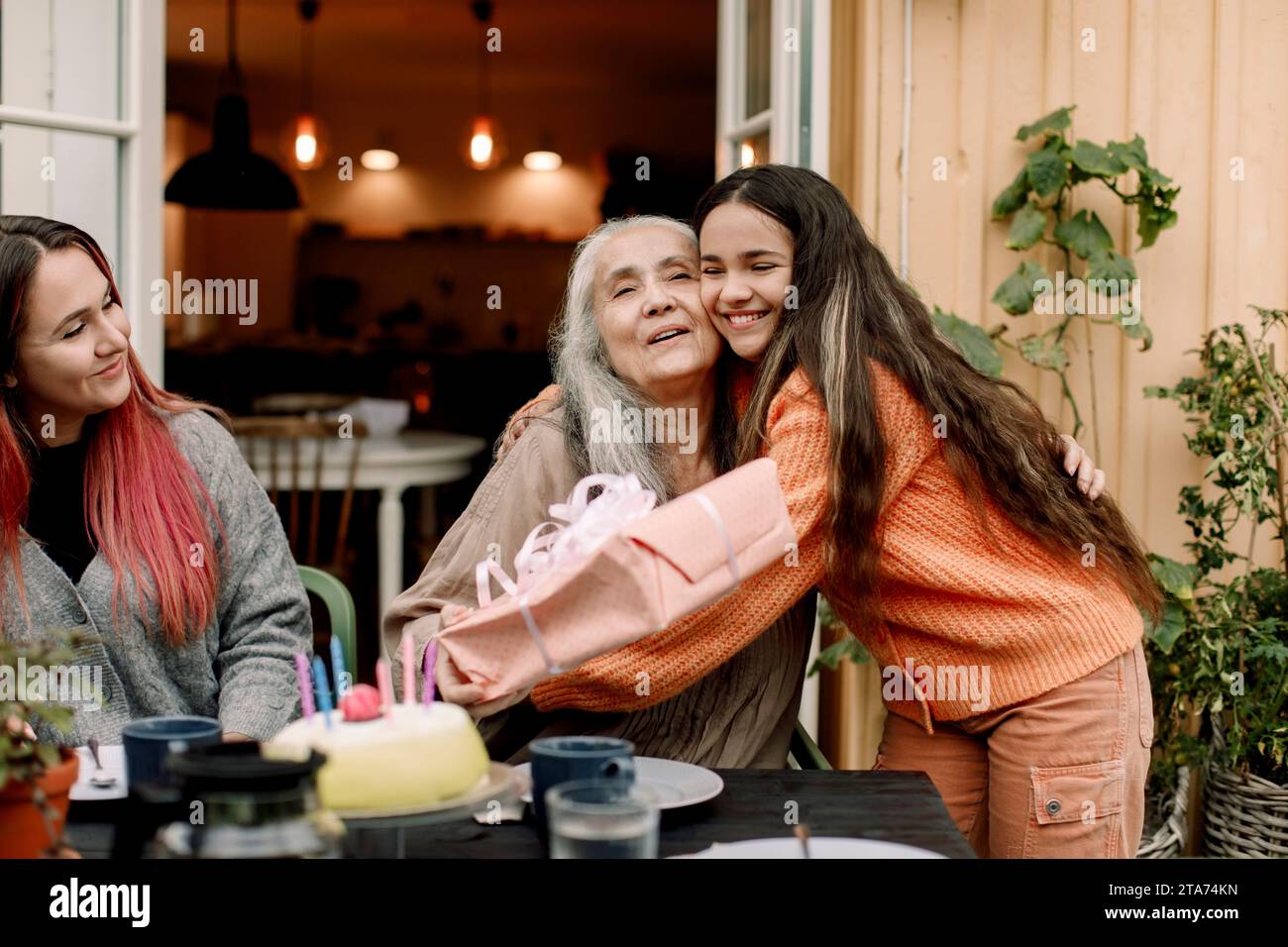Fille heureuse embrassant et souhaitant grand-mère à l'anniversaire au patio Banque D'Images