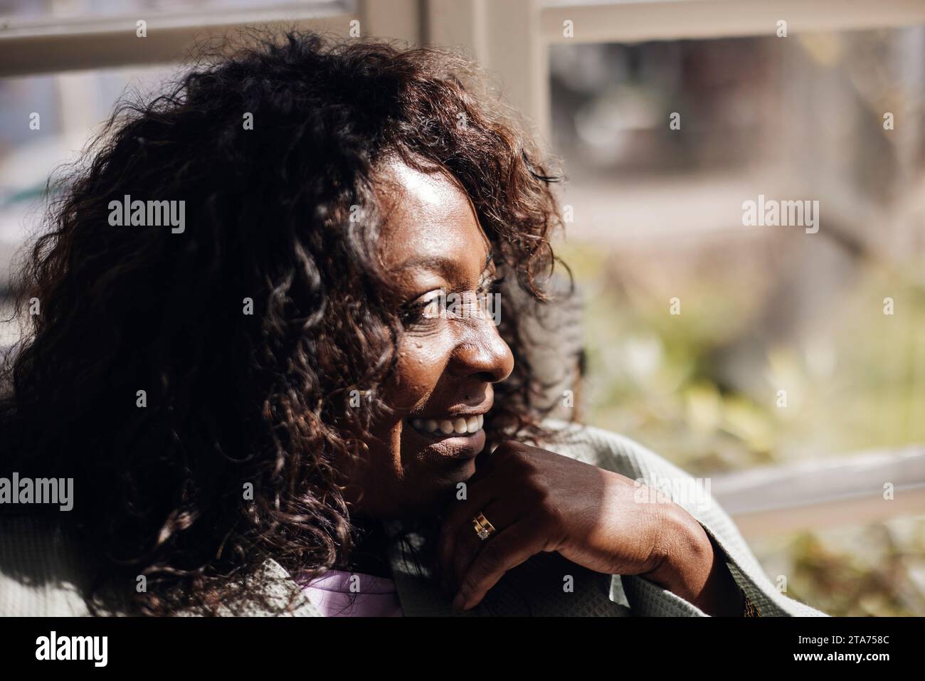 Heureuse femme mature avec les cheveux noirs regardant loin à la maison Banque D'Images