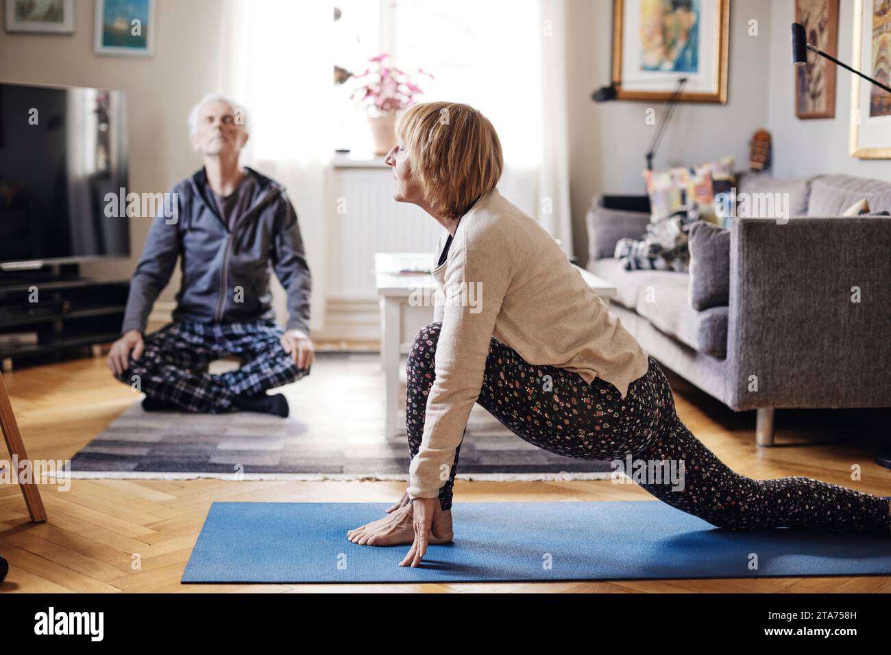 Femme senior et homme pratiquant le yoga ensemble dans le salon à la maison Banque D'Images