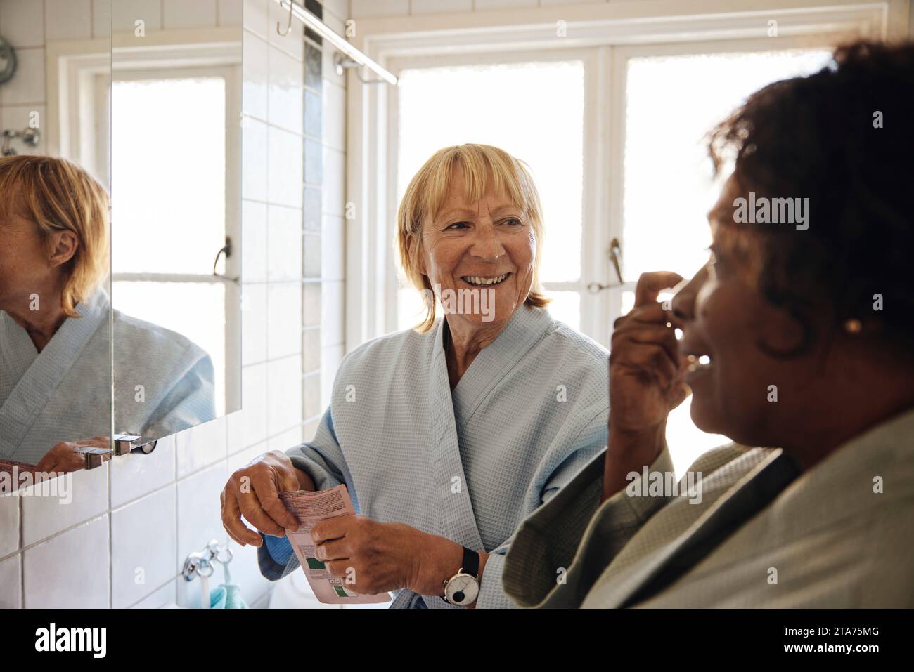 Femme blonde heureuse parlant à une amie féminine tout en faisant des soins de la peau dans la salle de bain à la maison Banque D'Images