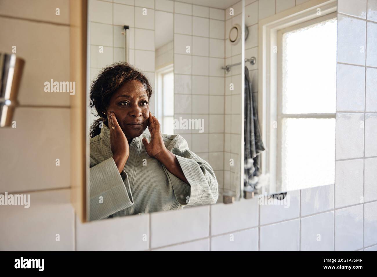 Femme mature touchant le visage tout en regardant dans le miroir dans la salle de bain à la maison Banque D'Images