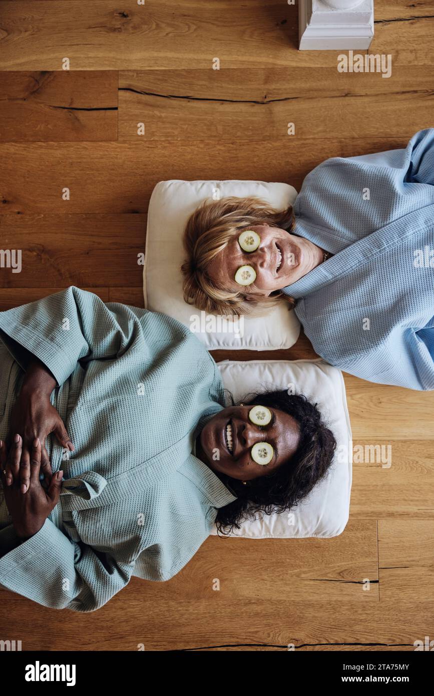 Directement au-dessus de la vue des amies souriantes avec des tranches de concombre sur les yeux se relaxant sur le sol à la maison Banque D'Images