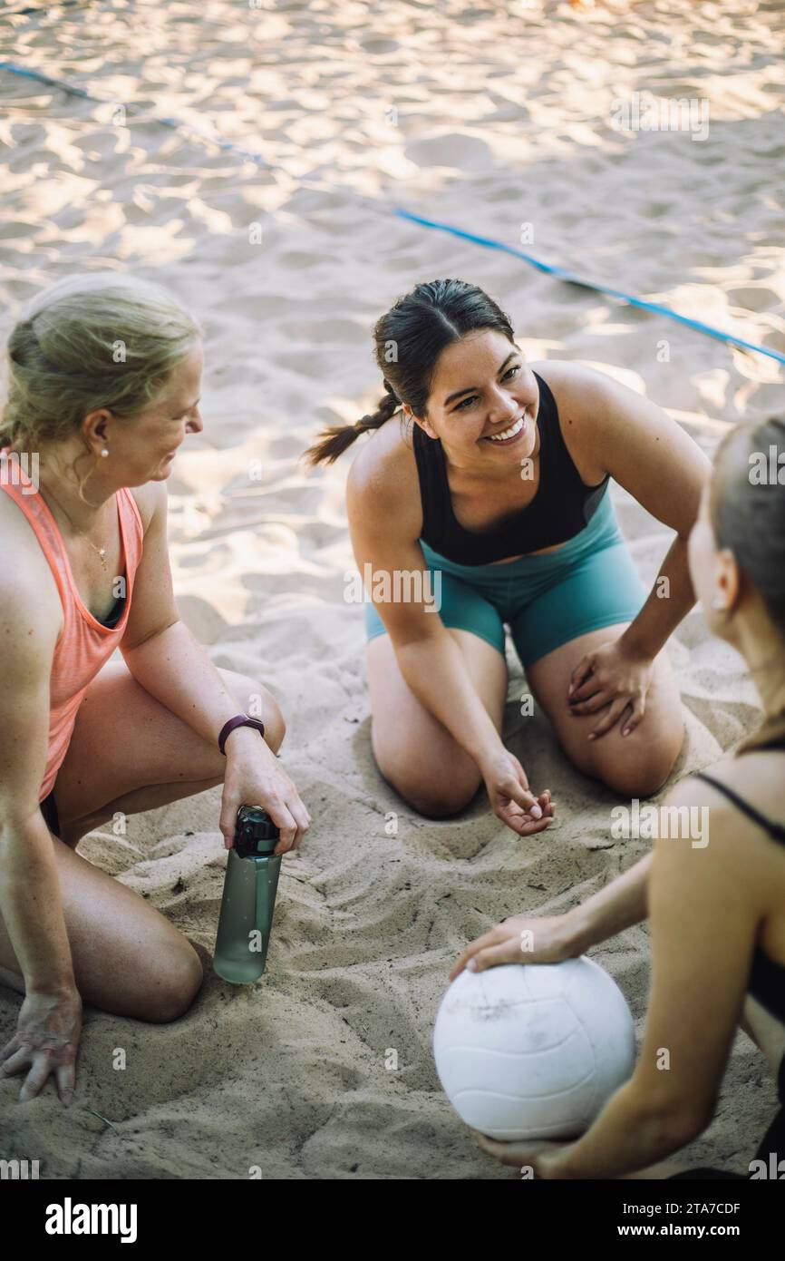 Femme souriante parlant avec des amis tenant le volley-ball sur le sable Banque D'Images