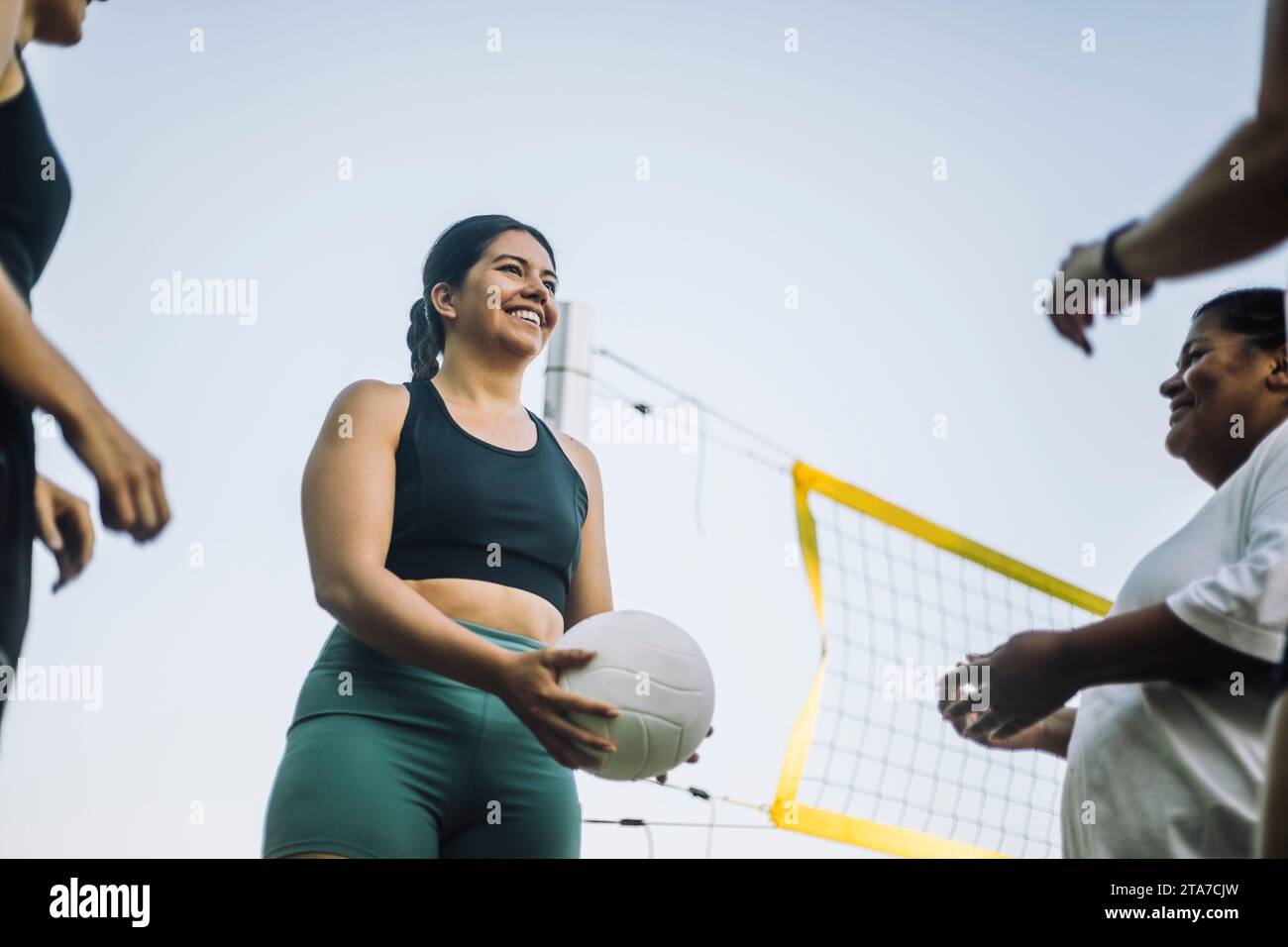 Vue à angle bas de femme souriante jouant au volleyball avec des amis contre le ciel Banque D'Images