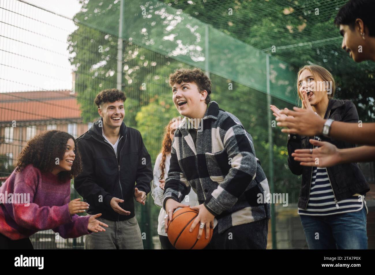Heureux amis acclamant adolescent garçon se préparant à prendre le tir tout en jouant au basket-ball sur le terrain Banque D'Images