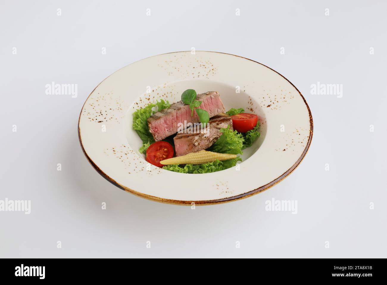 Steak de thon, laitue et légumes dans une belle assiette sur fond blanc, restaurant servant. Banque D'Images