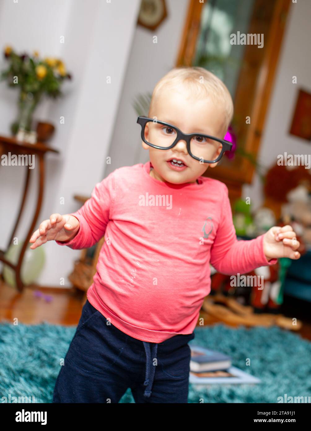 Bébé habillé en rose avec de grandes lunettes sans lentilles s'amuse autour de la maison et rit Banque D'Images