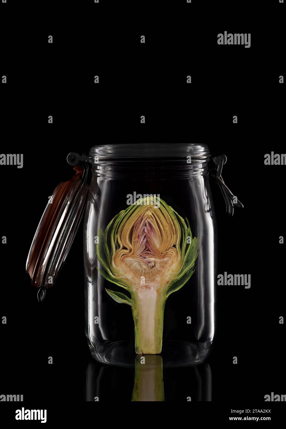 Un Artichaut dans un pot de stockage en verre ou de conserve isolé sur noir avec réflexion, avec couvercle ouvert. Banque D'Images