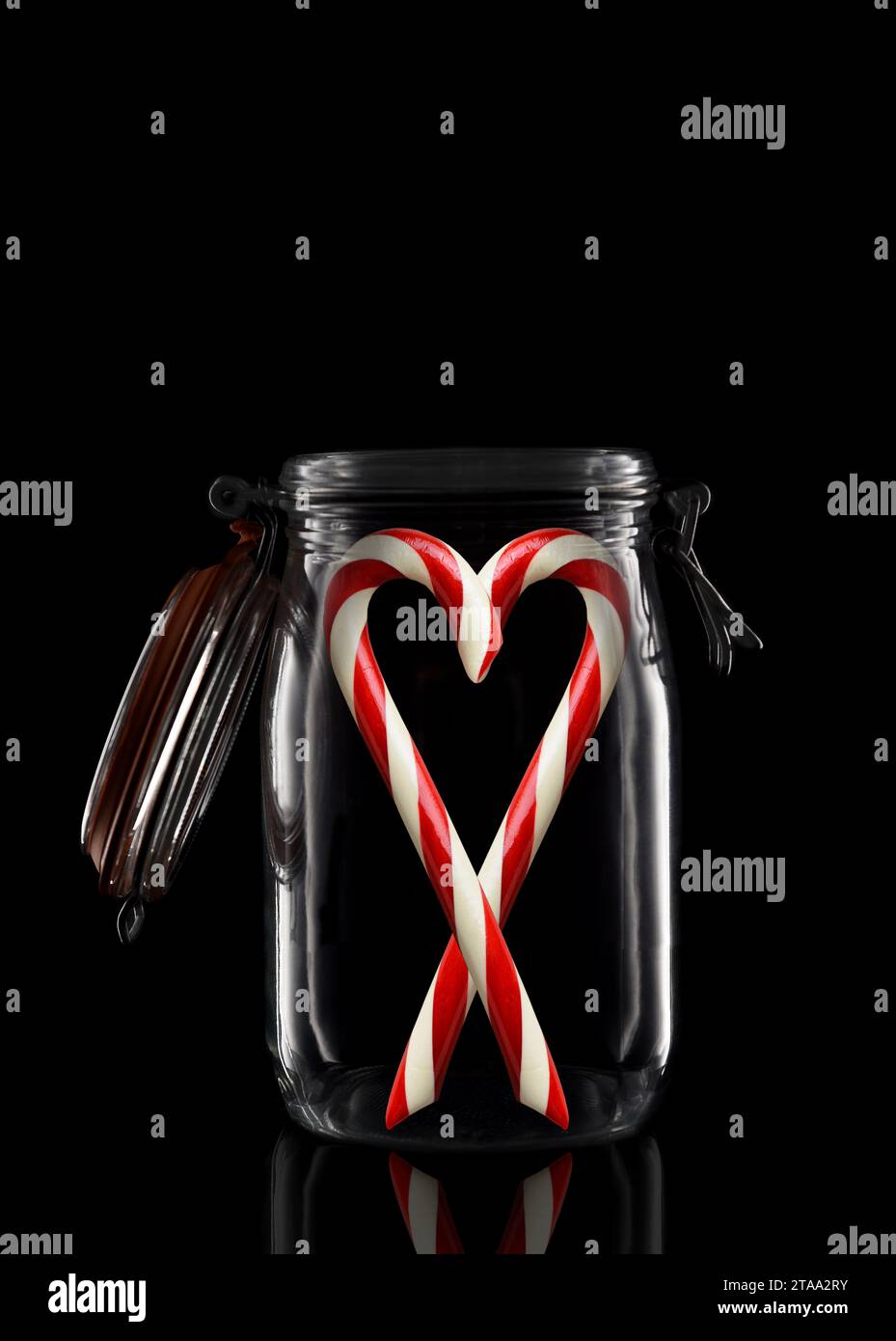 Deux cannes à sucre dans un pot de stockage en verre ou de mise en conserve isolé sur noir avec réflexion, avec couvercle ouvert. Banque D'Images