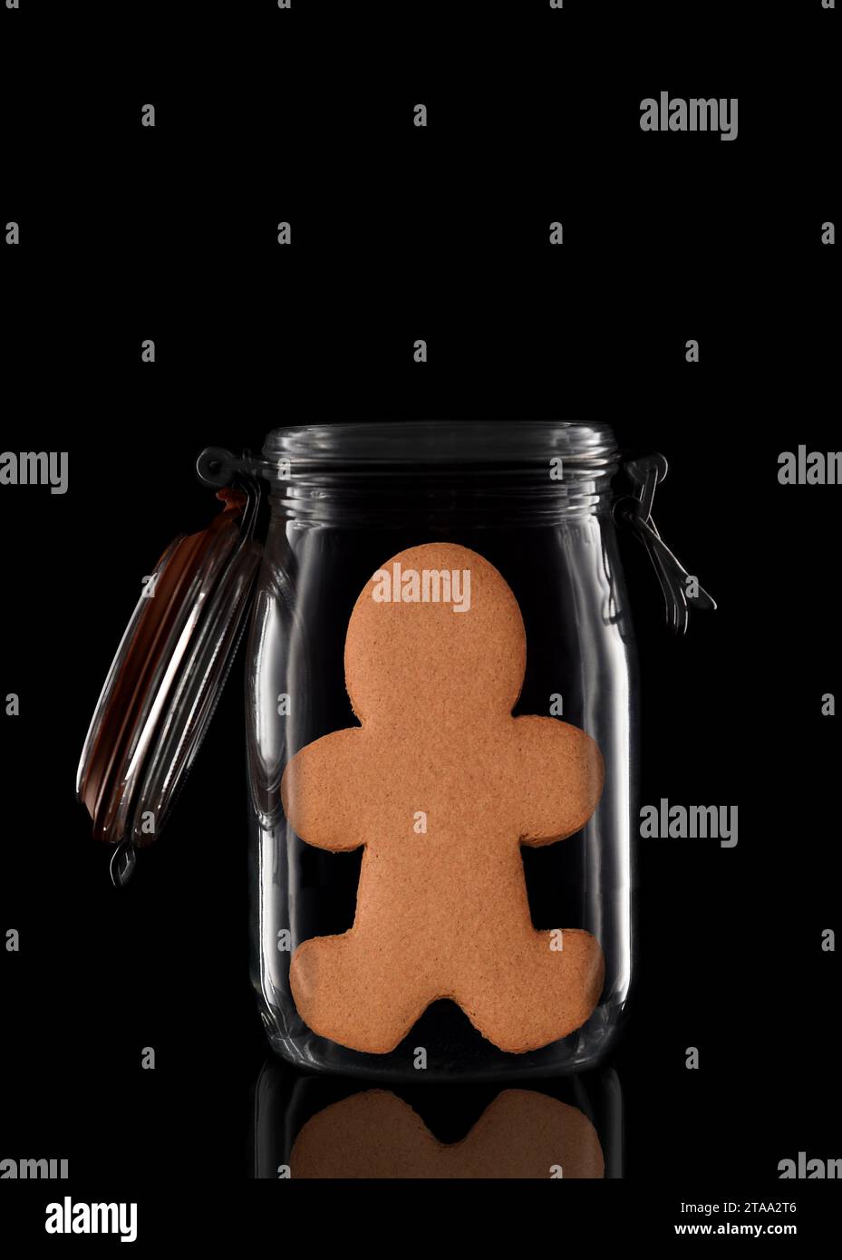 Un homme en pain d'épice dans un pot de stockage en verre ou de conserve isolé sur noir avec réflexion, avec couvercle ouvert. Banque D'Images