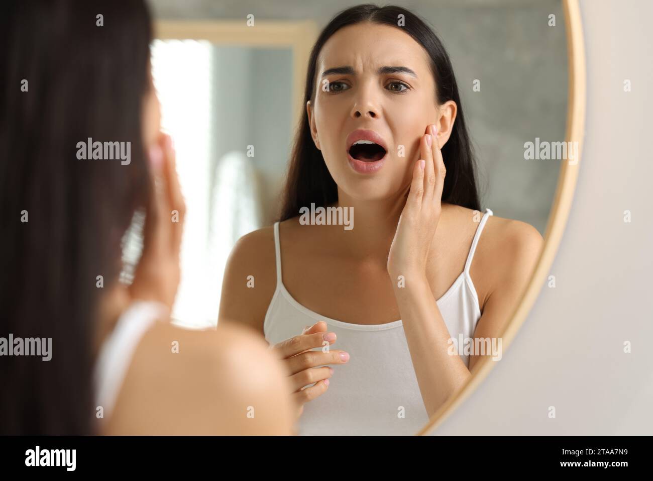 Souffrant d'allergie. Jeune femme émotive regardant sa peau irritée près du miroir à l'intérieur Banque D'Images