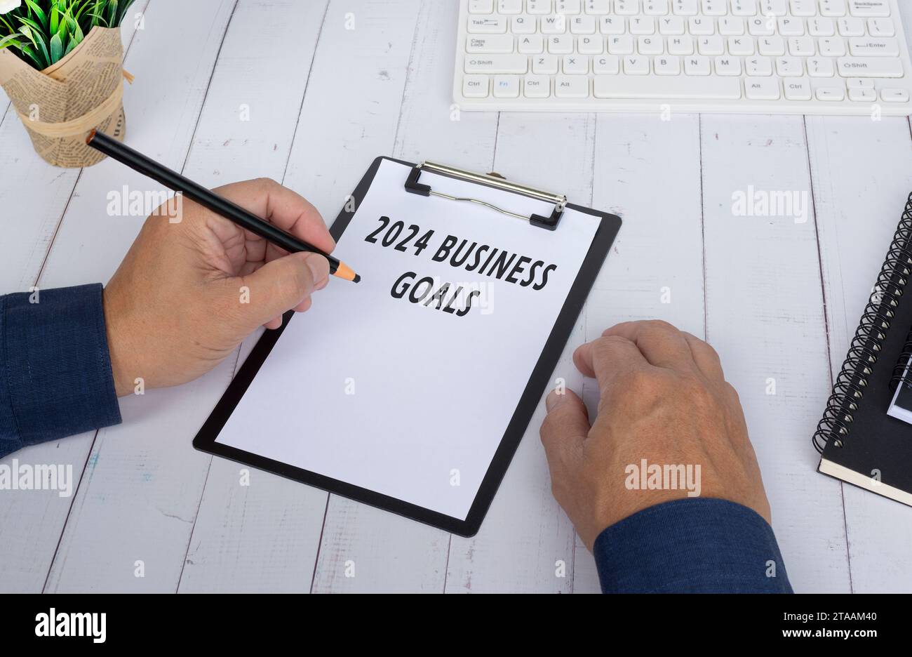Mains écrivant un 2024 objectifs d'affaires sur un tableau à pince sur un bureau en bois blanc. Concept commercial et financier. Banque D'Images