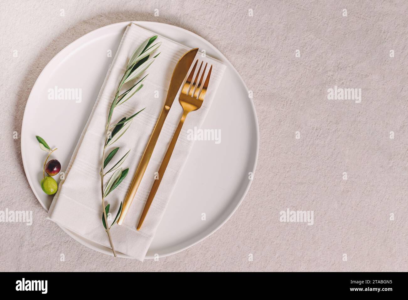 Assiette avec couverts de couleur dorée et branche d'olivier, élégant arrangement de table, vue de dessus Banque D'Images
