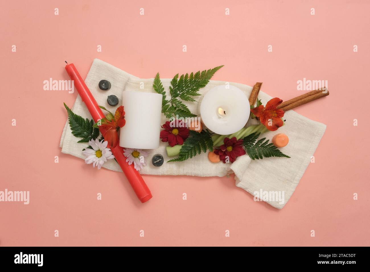 Bougies, fleurs fraîches, cannelle et feuilles vertes sont artistiquement décorées sur un fond rose avec un tissu blanc. Soyez créatif avec des bougies colorées Banque D'Images