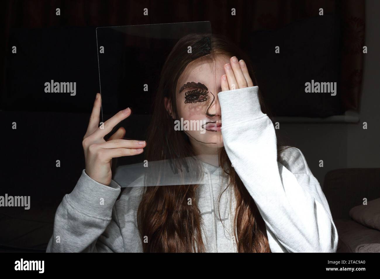 Adolescente tient une feuille transparent de perspex avec le dessin d'un demi-visage sur son propre visage pour montrer différentes émotions et sentiments Banque D'Images