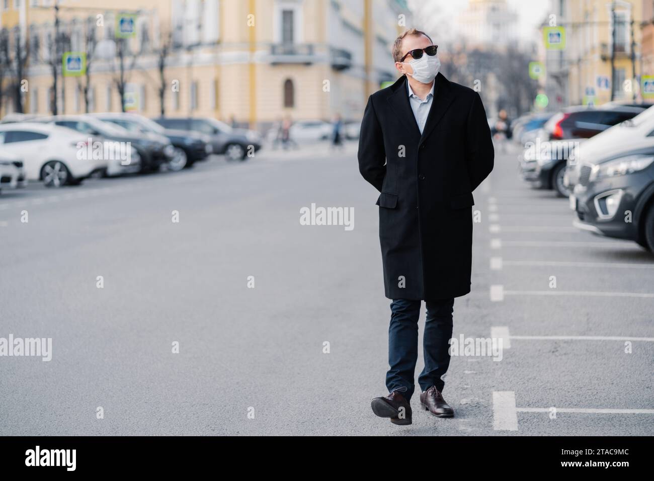 Homme marchant dans la ville portant un long manteau et un masque facial, pratiquant la sécurité sanitaire Banque D'Images