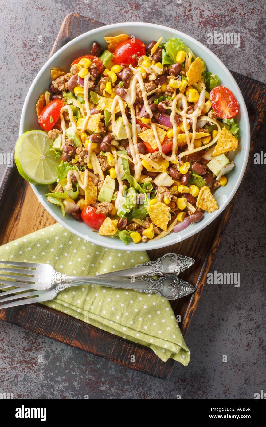 La salade Taco est une salade chaude à base de haricots piments, de bœuf haché épicé, de maïs, de laitue, de fromage et d'avocat en gros plan sur l'assiette de la table. Haut vertical Banque D'Images