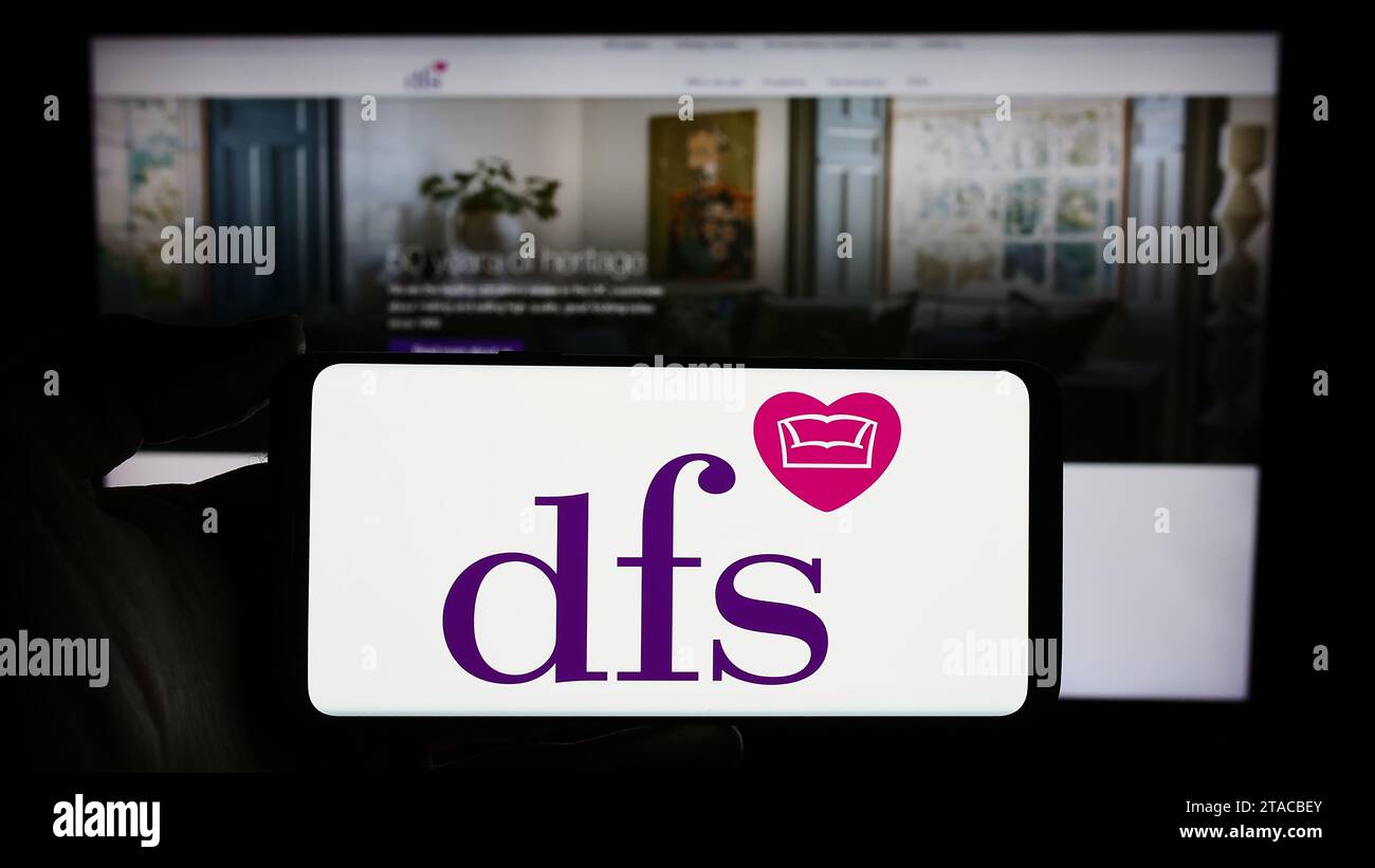 Personne détenant un smartphone avec le logo de la société de vente au détail britannique DFS Furniture plc devant le site Web. Concentrez-vous sur l'affichage du téléphone. Banque D'Images