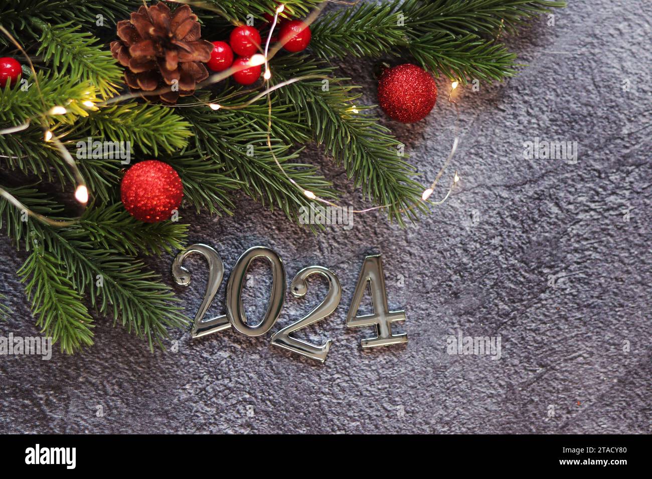 Bonne année 2024, fond gris avec branche de sapin et boules de Noël et guirlande lumineuse sur fond gris. Carte du nouvel an, bannière, vue de dessus, em Banque D'Images
