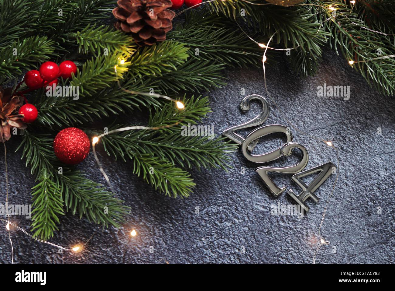 Bonne année 2024, fond gris avec branche de sapin et boules de Noël et guirlande lumineuse sur fond gris. Carte du nouvel an, bannière, vue de dessus, em Banque D'Images