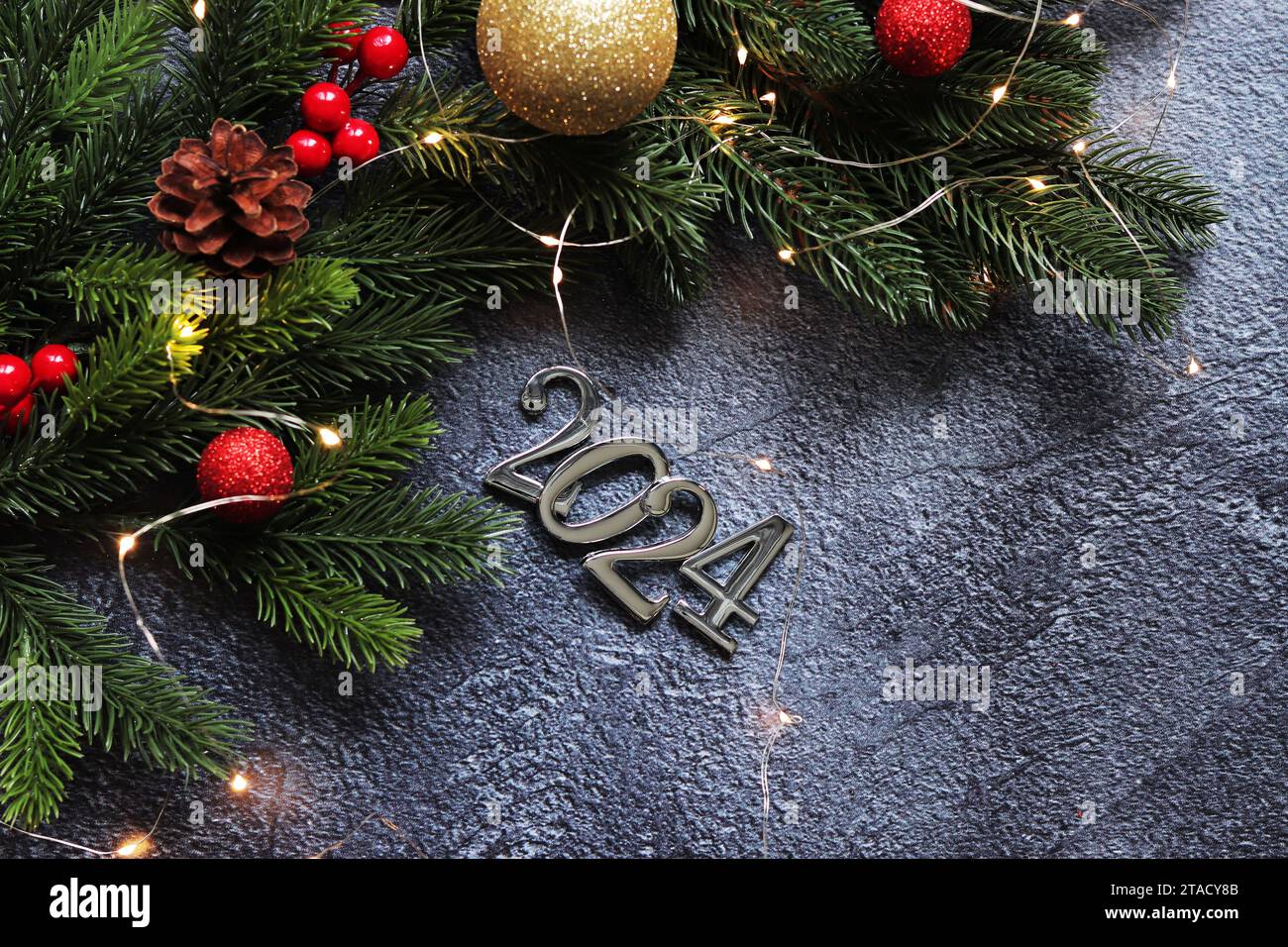 Bonne année 2024, fond gris avec branche de sapin et boules de Noël et guirlande lumineuse sur fond gris. Carte du nouvel an, bannière, vue de dessus, em Banque D'Images
