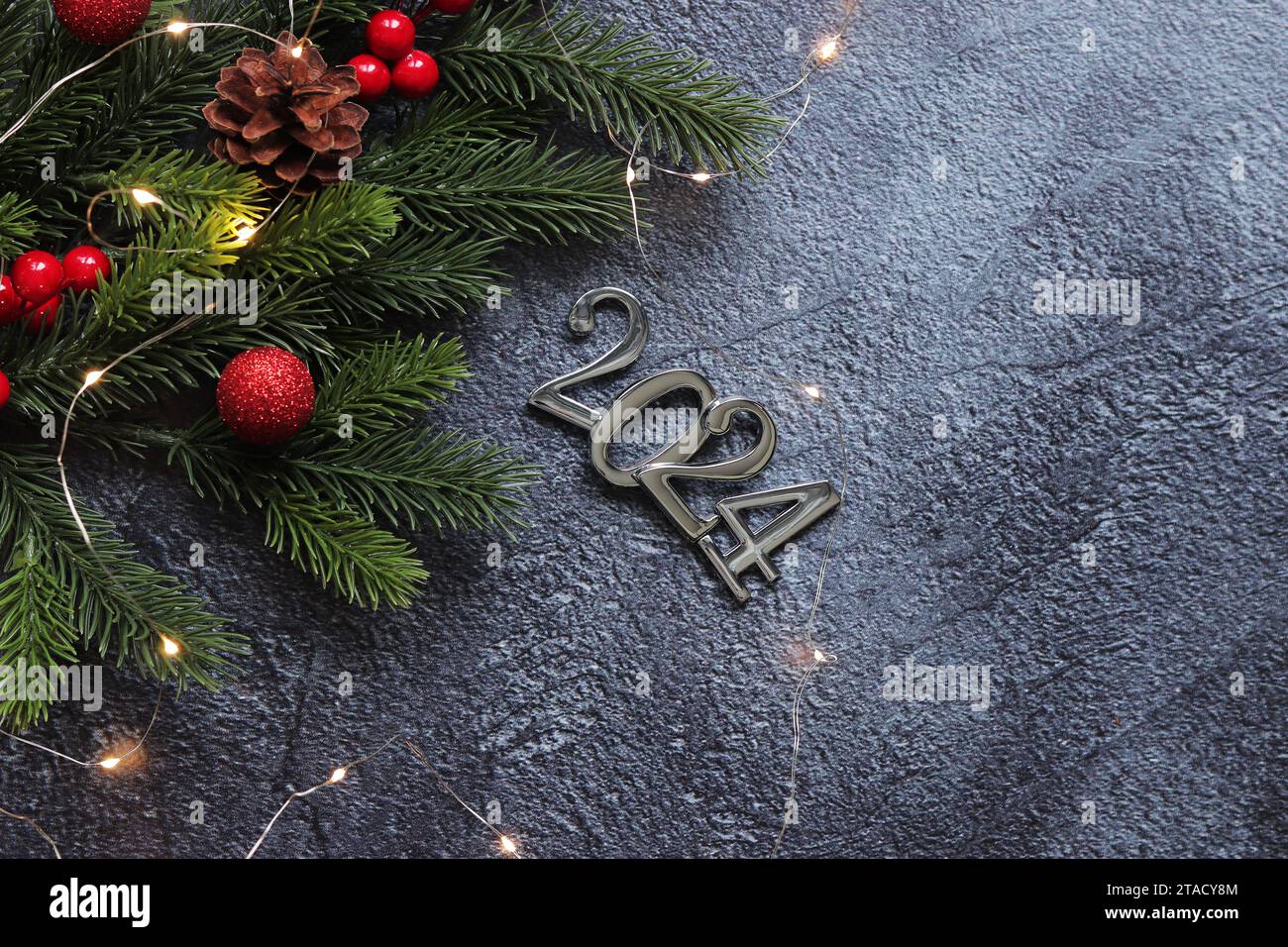 Bonne année 2024, fond gris avec branche de sapin et boules de Noël et guirlande lumineuse sur fond gris. Carte du nouvel an, bannière, vue de dessus, em Banque D'Images