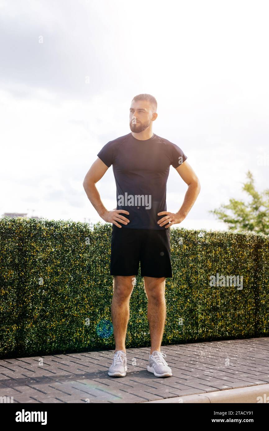 Jeune homme en sportswear debout avec ses mains sur ses hanches après une séance d'entraînement ou après avoir couru. Homme athlétique prendre une pause après la formation.Fitness Banque D'Images