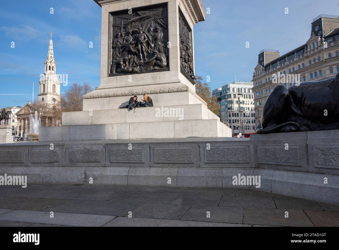 Deux jeunes femmes assises sur les marches au pied de la colonne Nelson, Trafalgar Square, Londres Banque D'Images