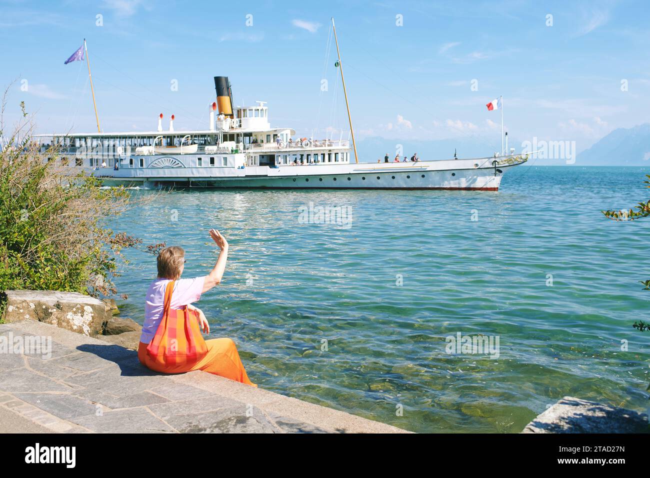 Portrait en plein air d'une femme âgée de 50 - 55 ans assise au bord du lac, regardant flotter bateau français suisse sur le lac Genève, Suisse Banque D'Images