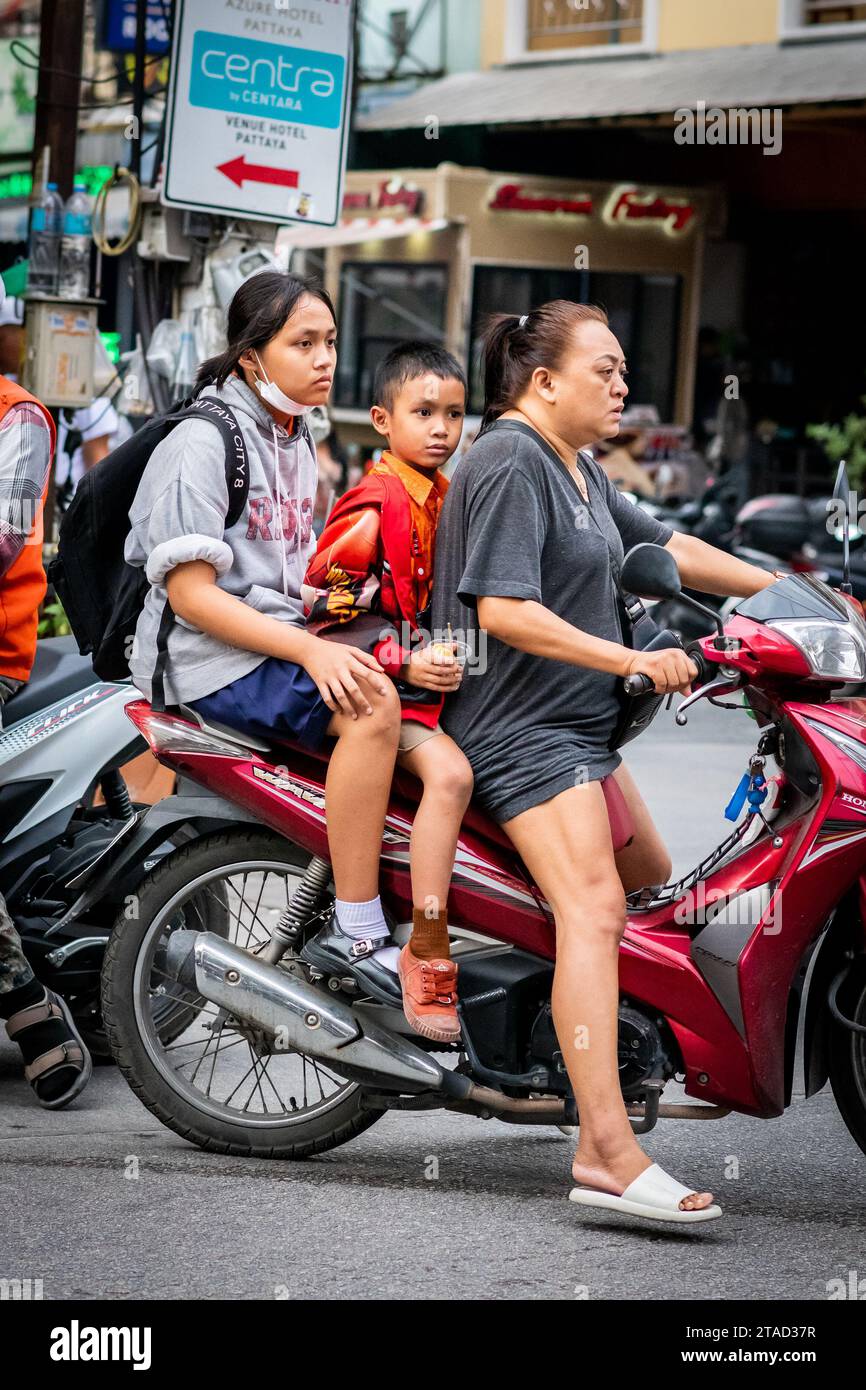 Deux enfants thaïlandais voyagent à travers les rues animées de la ville de Pattaya, en Thaïlande, à l'arrière d'une moto. Banque D'Images