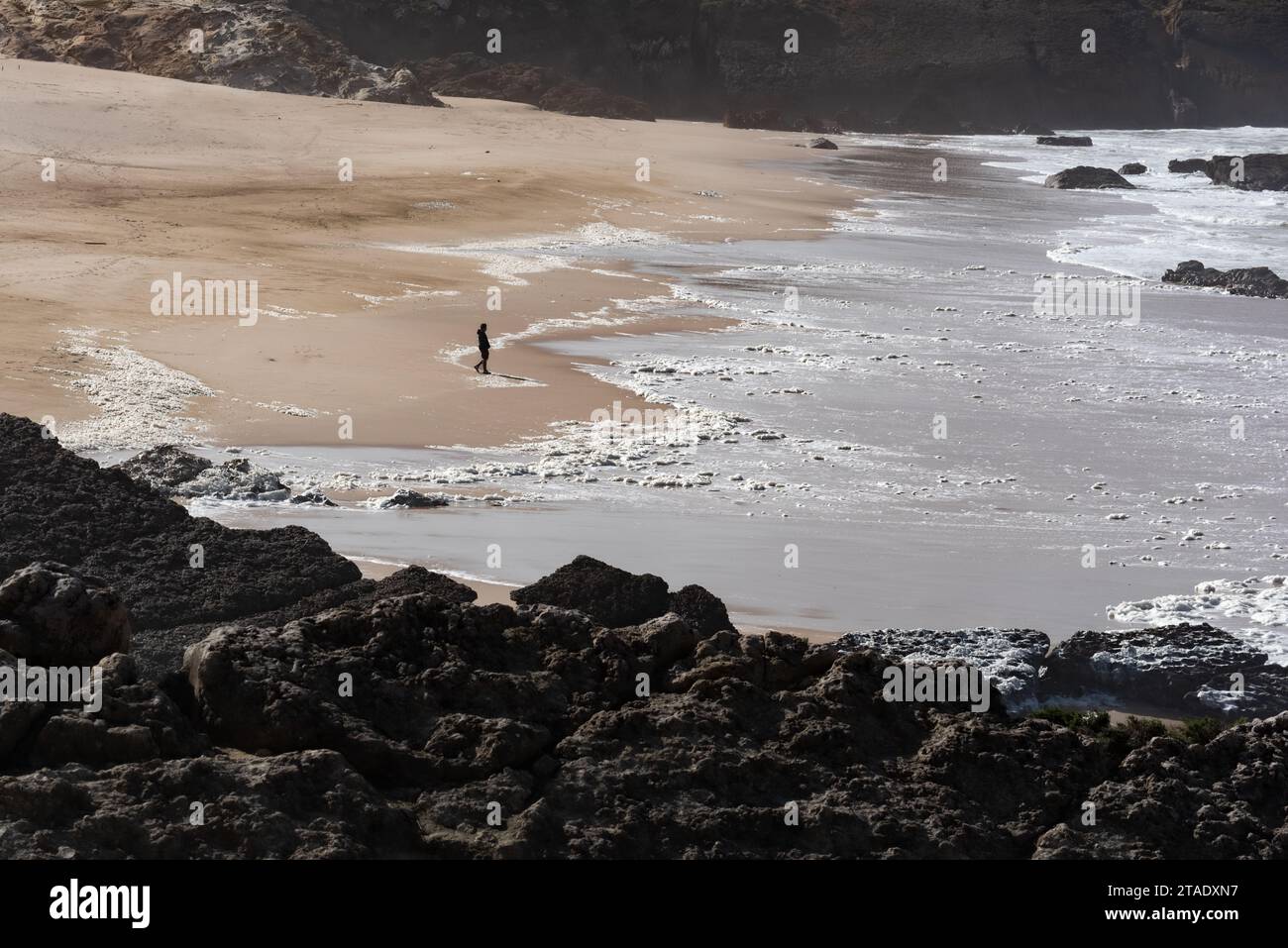 Une silhouette d'une seule personne approchant le bord de l'océan sur une plage de sable vide de Cresmina en basse saison à Cascais au Portugal Banque D'Images