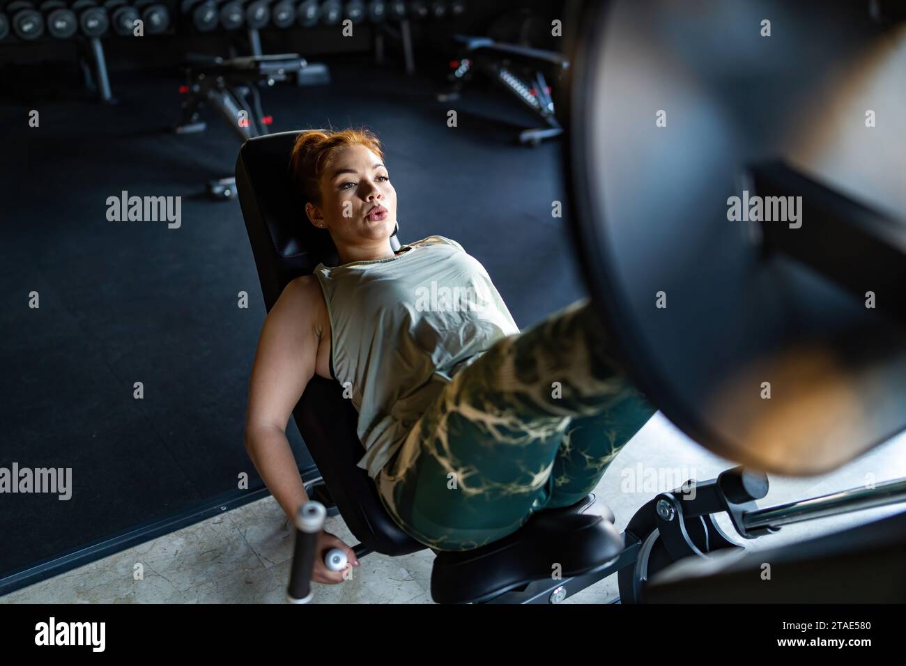 Femme concentrée s'engageant dans un exercice de presse de jambe intense, poussant des poids sur une machine de gym pour la forme physique. Banque D'Images