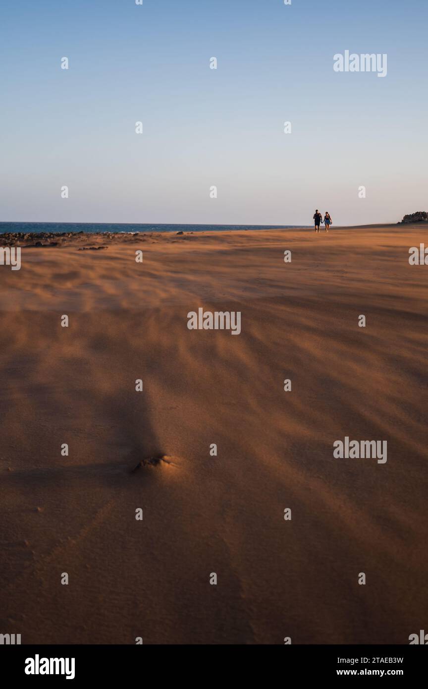 Couple marche sur la plage comme un vent fort souffle le sable à Lanzarote, îles Canaries, Espagne Banque D'Images