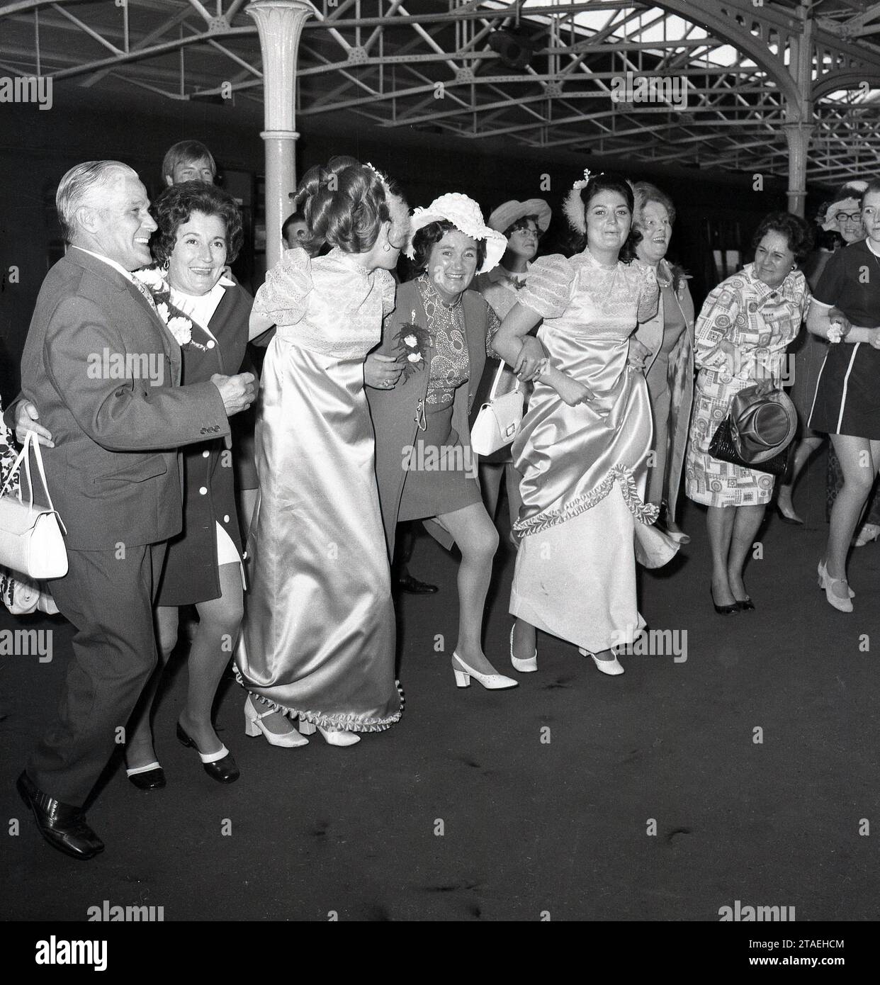 Années 1960, histoire, mariage amusant..., invités excités, menés par les deux demoiselles d'honneur, joignent les bras sous les arches de la gare de Vauxhall pour donner à la mariée et au marié - hors caméra sur un wagon - un grand envoi pour la lune de miel, Angleterre, UK.England, Royaume-Uni. Banque D'Images