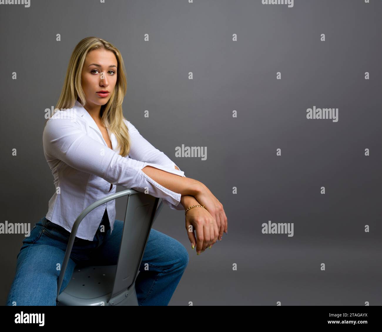 Brawny Body Builder Belle jeune femme expression réfléchie assise face à la caméra gris fond gris Copy Space Banque D'Images