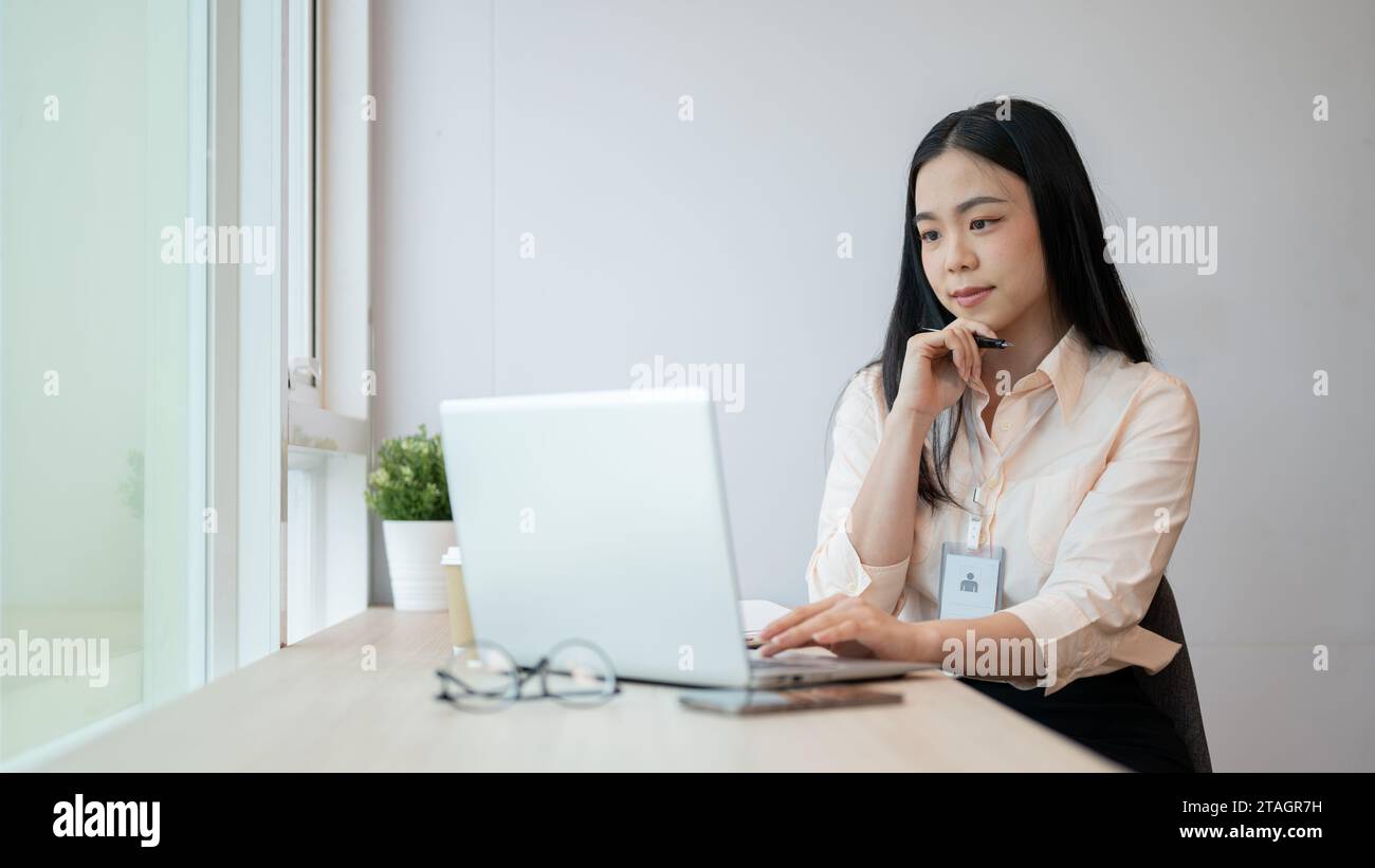 Une femme d'affaires asiatique spécialisée et professionnelle travaille sur son ordinateur portable au bureau, pensant et planifiant un nouveau projet. Banque D'Images