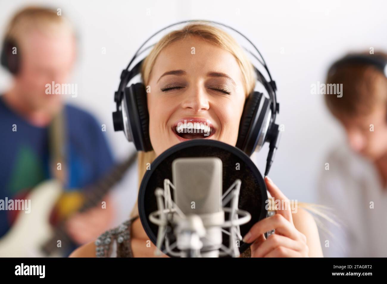 Femme heureuse, chanteuse et microphone avec casque dans le studio d'enregistrement de musique, piste sonore ou podcast. Personne féminine, blonde ou musicien sourire au micro Banque D'Images