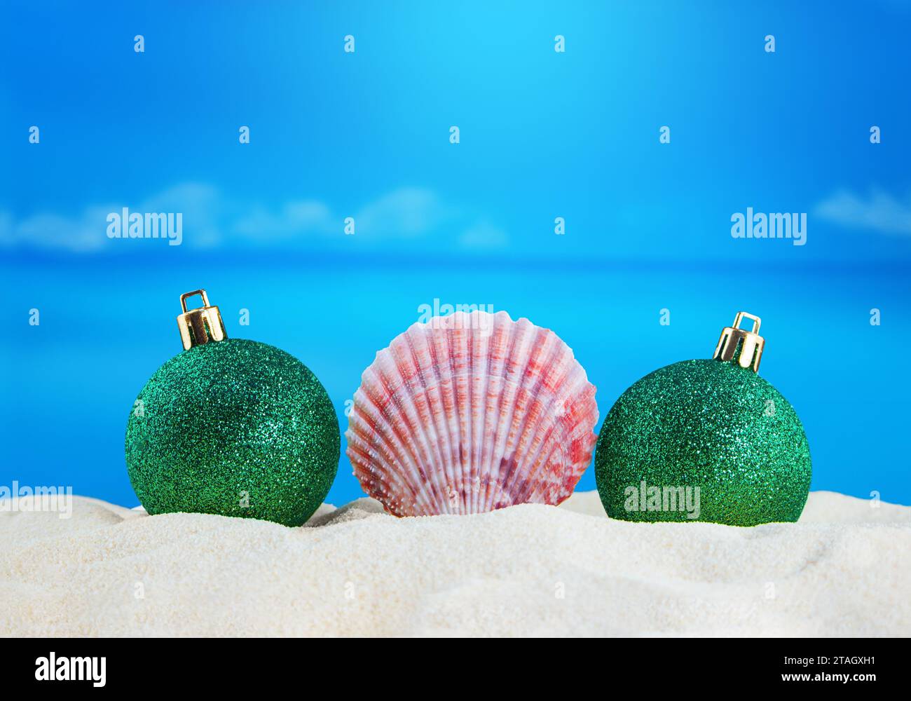 Conque rose avec des boules vertes brillantes de Noël sur le sable de la plage avec mer. Nouvel an, vacances. Espace de copie Banque D'Images