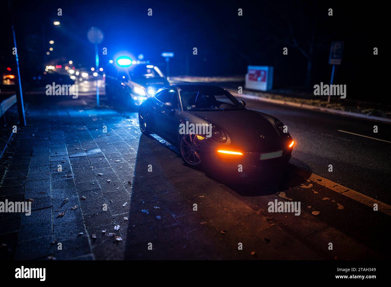 Ein Streifenwagen der Polizei mit eingeschalteten Blaulicht hinter einem Porsche Carrera 911 S4 nach einem Verkehrsunfall mit Bagatellschaden. Banque D'Images