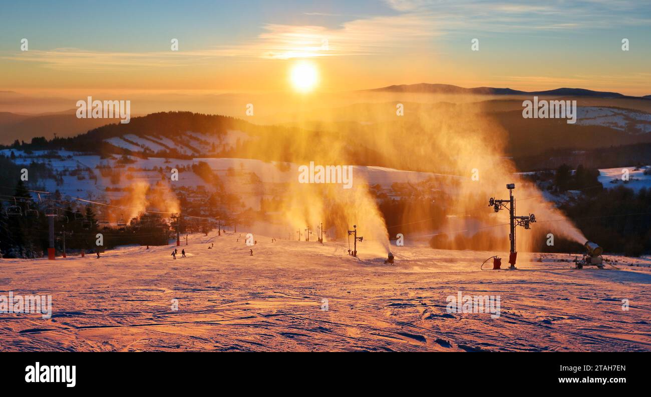 Piste de ski dans la station d'hiver avec des skieurs et des canons à neige au coucher du soleil, Slovaquie Banque D'Images